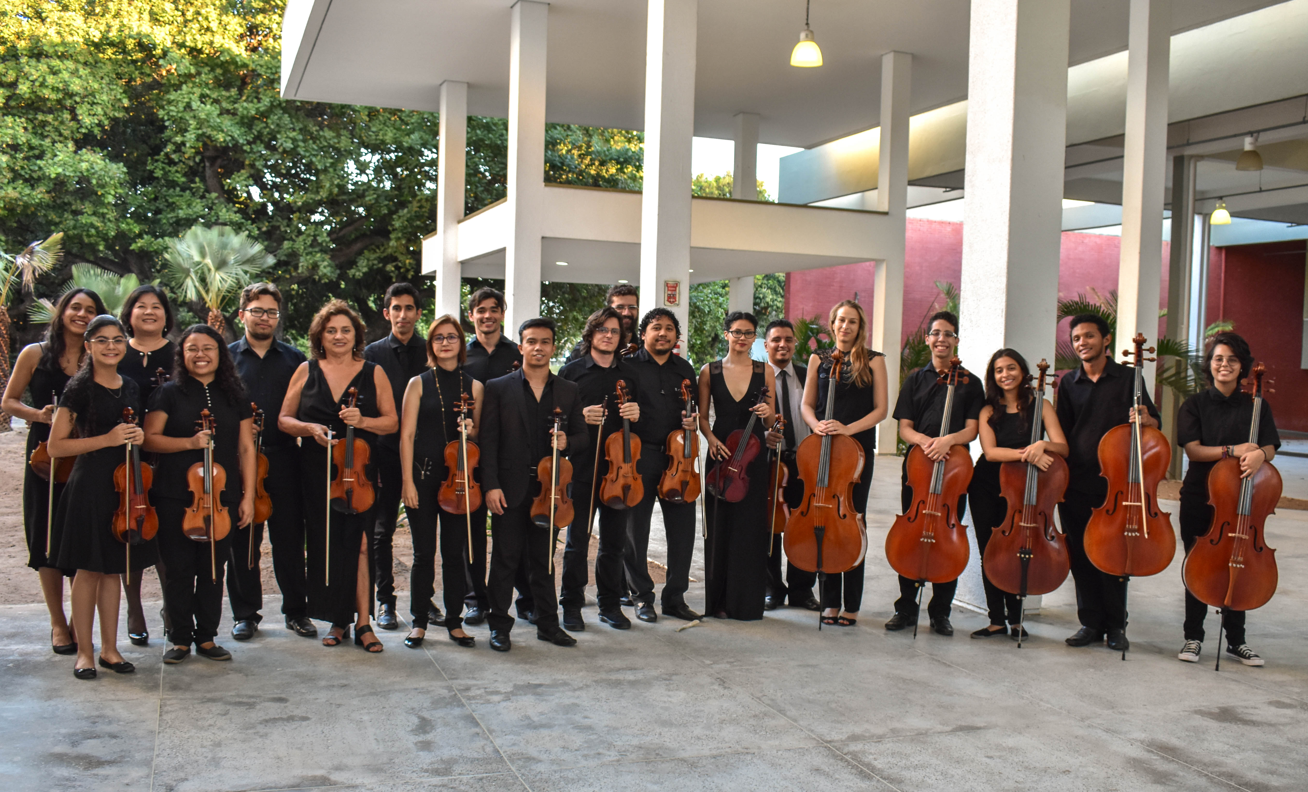 Músicos da Camerata de Cordas da UFC estão alinhados e vestindo preto, posando com seus instrumentos de cordas, violinos e violoncelos